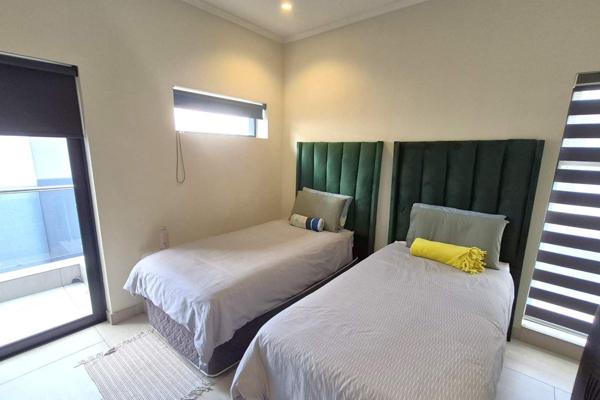 A well-maintained bedroom featuring tiled flooring, recessed lighting, modern roller blinds, and a sliding glass door providing access to an outdoor balcony area.