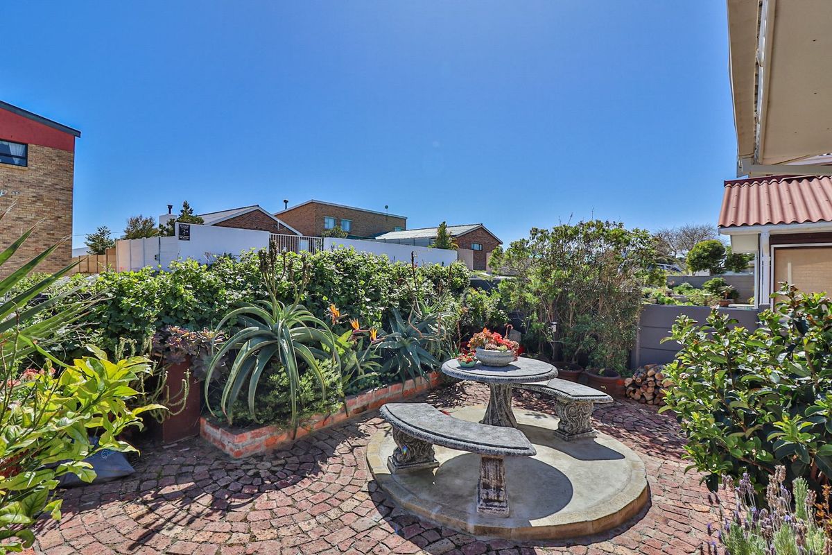 A well-maintained rear garden area featuring a circular brick-paved patio, raised garden beds, and established landscaping.