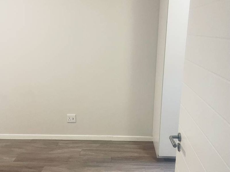 A clean, empty bedroom featuring modern laminate flooring and a built-in cupboard, offering a neutral canvas for personalization.