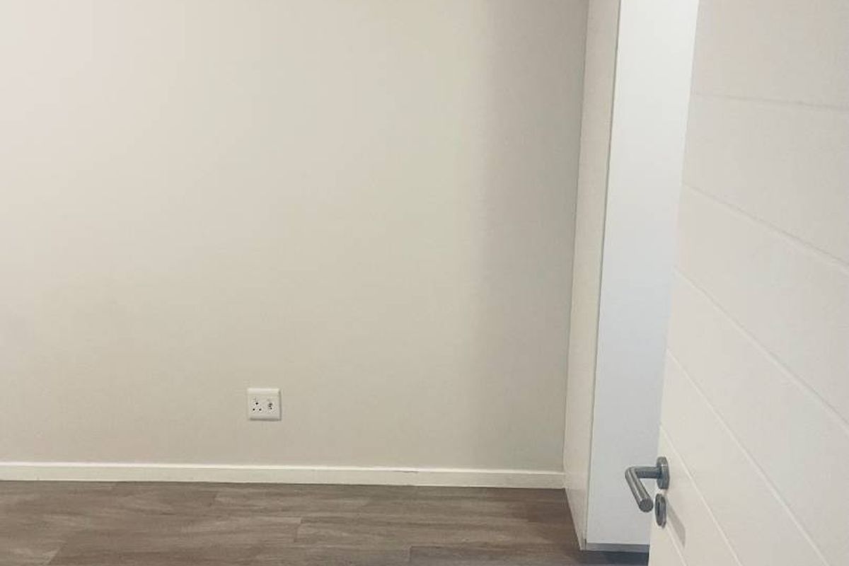 A clean, empty bedroom featuring modern laminate flooring and a built-in cupboard, offering a neutral canvas for personalization.