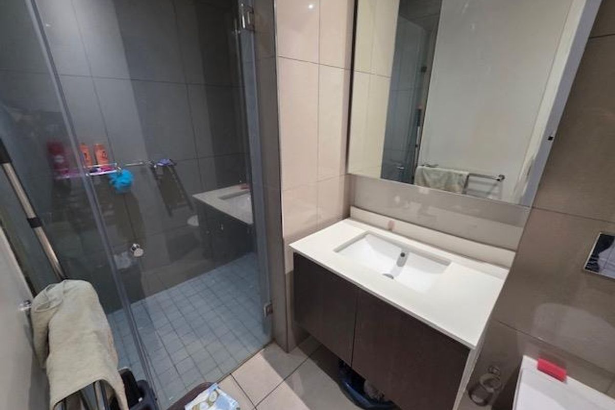 Modern bathroom featuring a vanity cabinet with integrated sink, wall-mounted mirror, glass shower enclosure, and wall-mounted toilet with neutral tiled finishes.