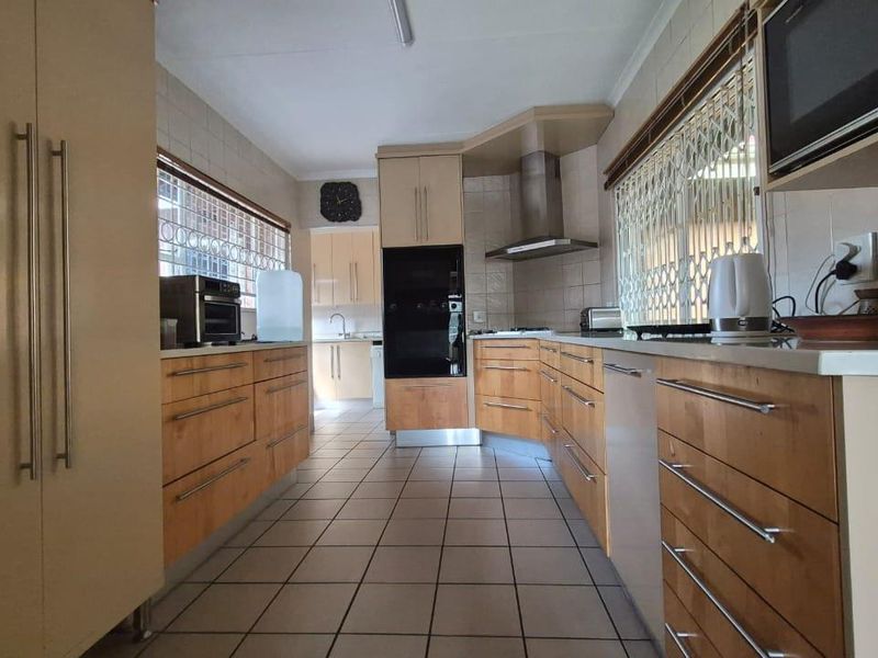 A functional kitchen featuring wooden cabinetry, built-in oven, extractor fan, tiled flooring, and tiled backsplash with security gates on the windows.