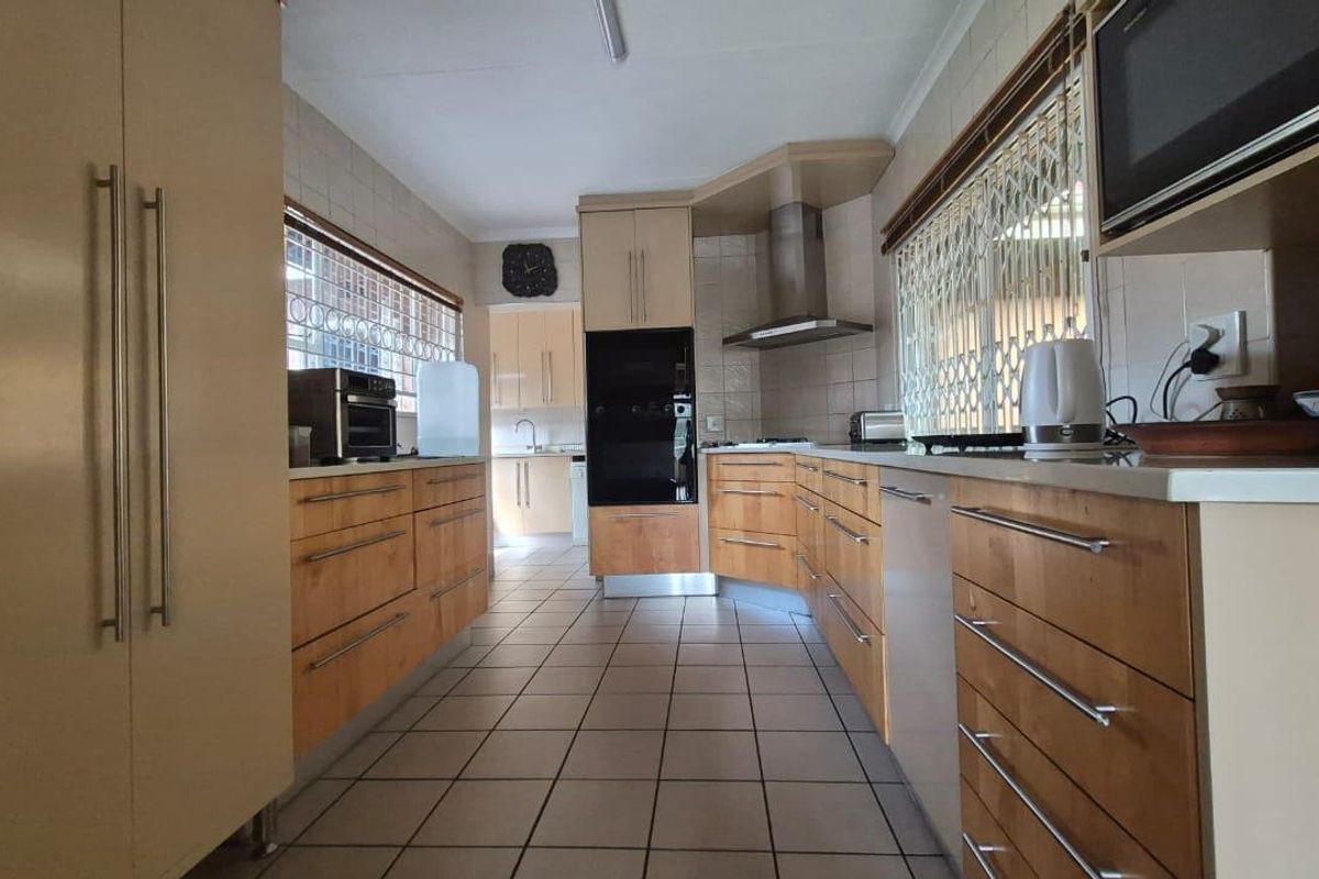 A functional kitchen featuring wooden cabinetry, built-in oven, extractor fan, tiled flooring, and tiled backsplash with security gates on the windows.