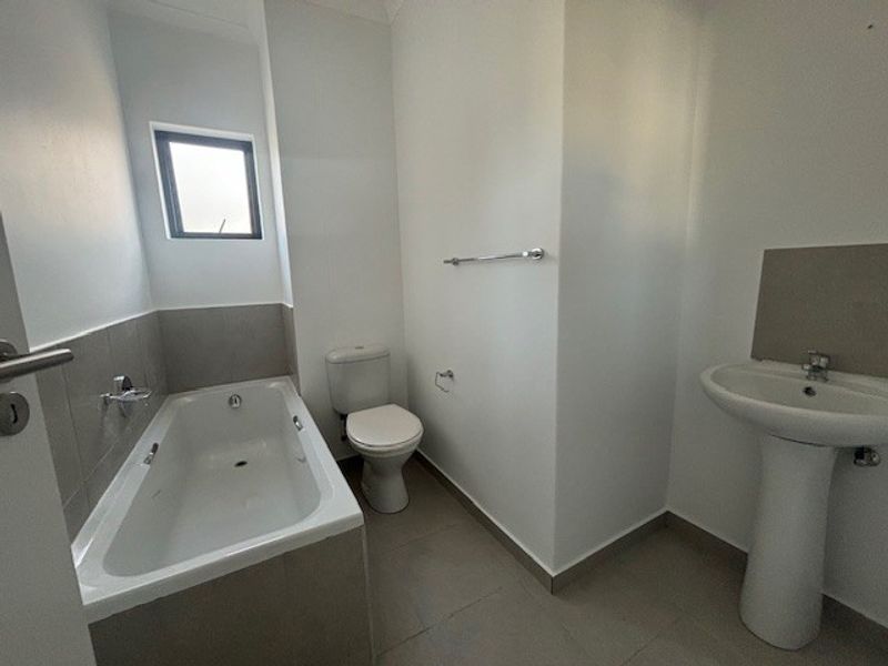 A clean and functional bathroom featuring a bathtub, pedestal basin, and toilet with neutral tiling and modern fixtures.