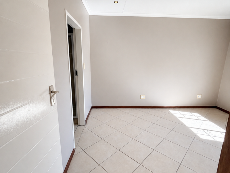 A bright, empty bedroom featuring neutral wall tones, tiled flooring, and recessed ceiling lighting, providing a clean canvas for personalization.