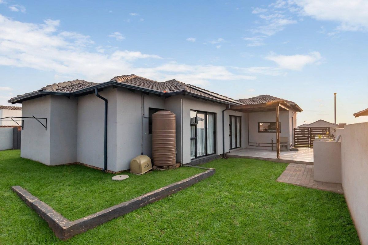 Rear view of the property featuring a covered patio with a timber pergola, a water storage tank, and a landscaped garden area.