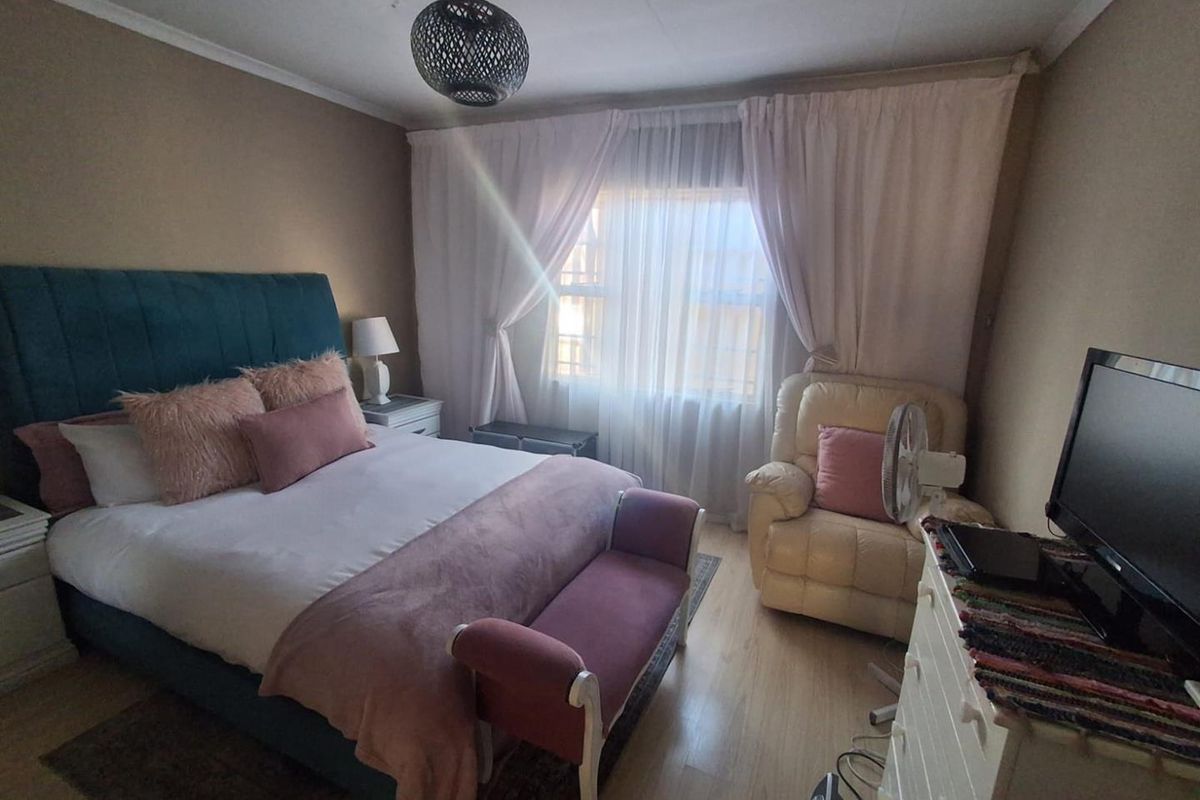 A cozy bedroom featuring laminate flooring, a large window with curtains, and a central light fixture.
