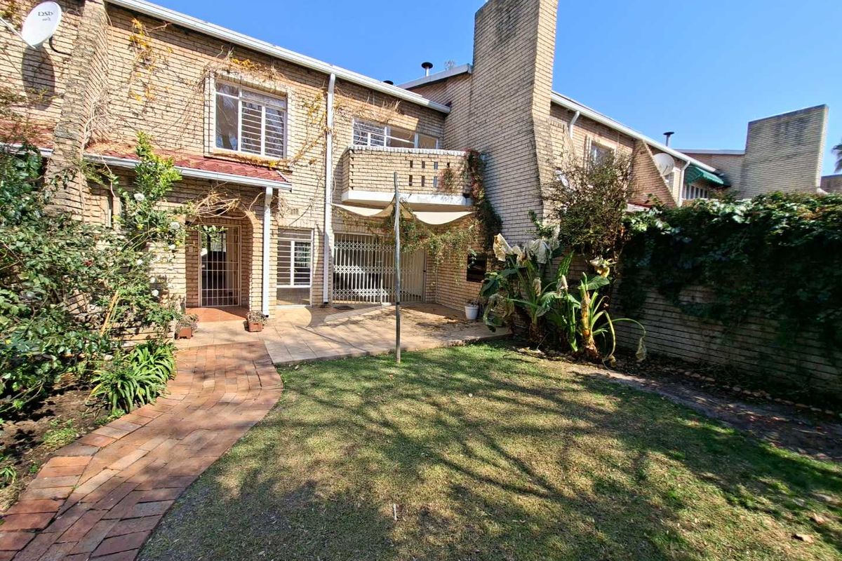 Rear view of a brick townhouse featuring a paved patio, small garden, and an upper-level balcony with security gates.