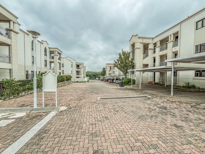 Exterior view of the apartment complex featuring paved parking areas, covered carports, and multi-story residential buildings with balconies.