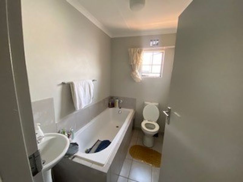 A functional bathroom featuring a pedestal basin, built-in bathtub, and toilet with neutral wall finishes and tiled flooring.