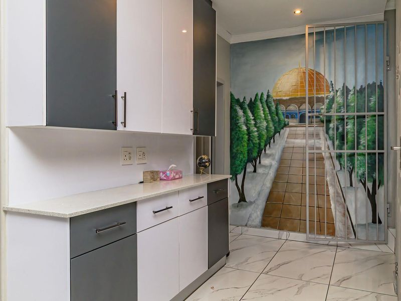 A modern scullery or utility area featuring two-tone cabinetry, stone countertops, tiled flooring, and a secure metal gate.