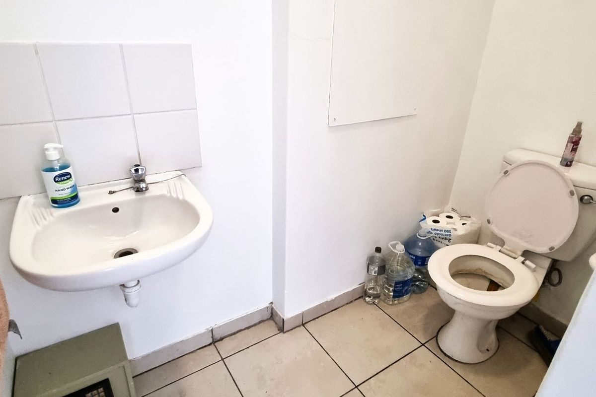 A functional office restroom featuring a wall-mounted basin with tiled splashback and a standard toilet suite.