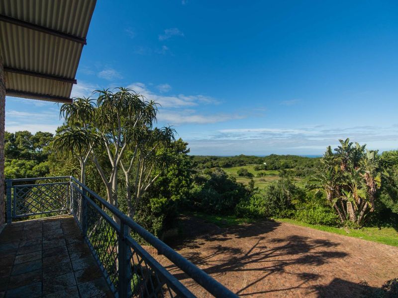 A spacious elevated balcony featuring a metal balustrade and tiled flooring, offering expansive views over the surrounding garden and natural landscape.