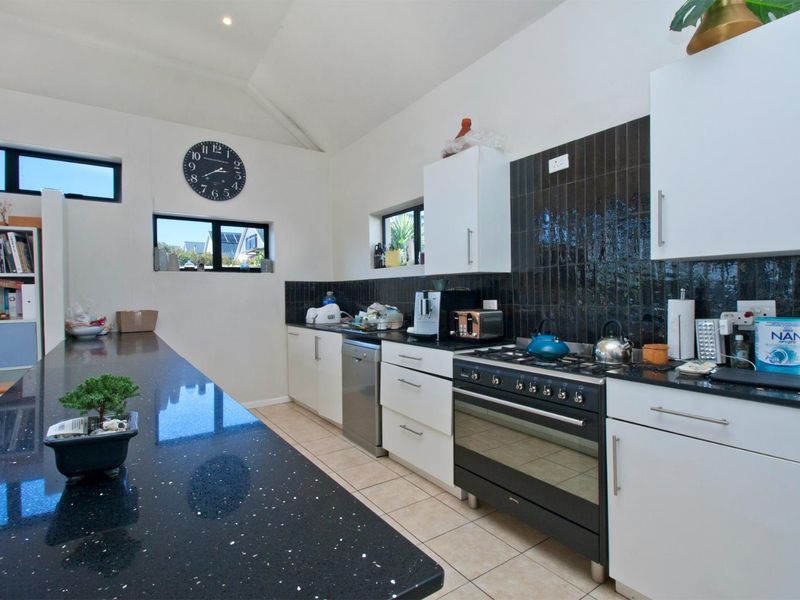 Modern kitchen featuring black granite countertops, a gas stove with oven, tiled splashback, and ample built-in cabinetry.