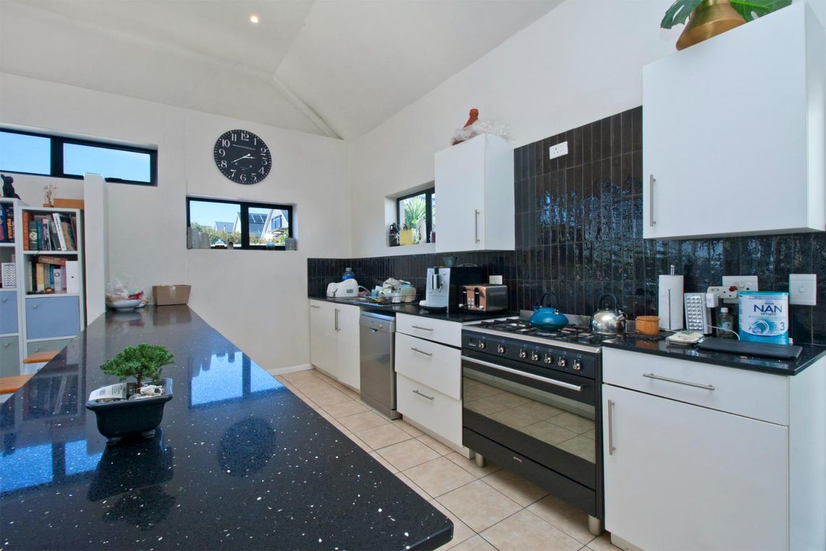 Modern kitchen featuring black granite countertops, a gas stove with oven, tiled splashback, and ample built-in cabinetry.