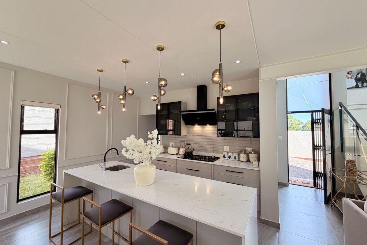 Modern kitchen featuring a large quartz-topped island, sleek cabinetry, gas hob with extractor, and elegant pendant lighting, creating a sophisticated and functional culinary space.