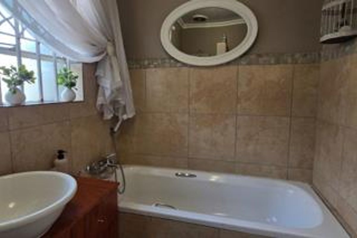 A bathroom featuring a built-in bathtub with tiled surround, a vanity basin, and a wall-mounted mirror.