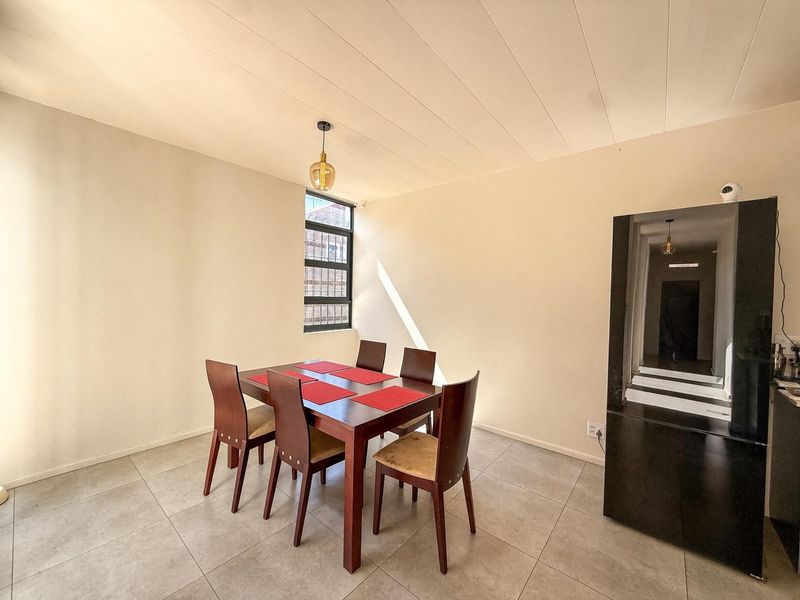 A dining area featuring tiled flooring, a pendant light, and a window with security bars, providing a functional space for meals.