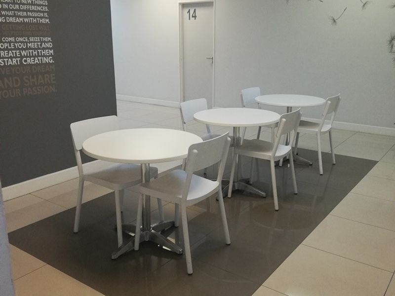 A bright office break area featuring tiled flooring, suspended ceilings with recessed lighting, and a neutral color palette with a feature wall.