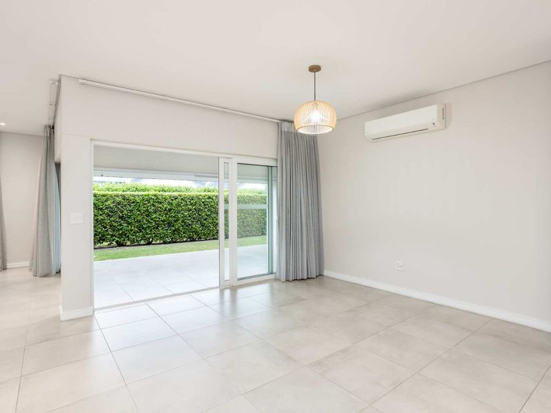 Bright and spacious living area featuring large sliding glass doors leading to a patio, neutral tiled flooring, and a wall-mounted air conditioning unit.