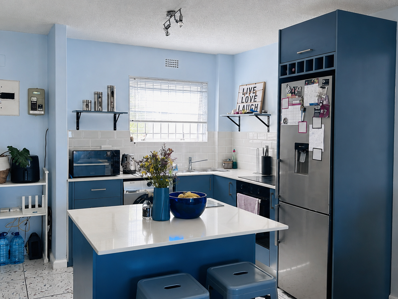 A functional kitchen featuring blue cabinetry, a central island with a quartz countertop, subway tile backsplash, and integrated stainless steel appliances.