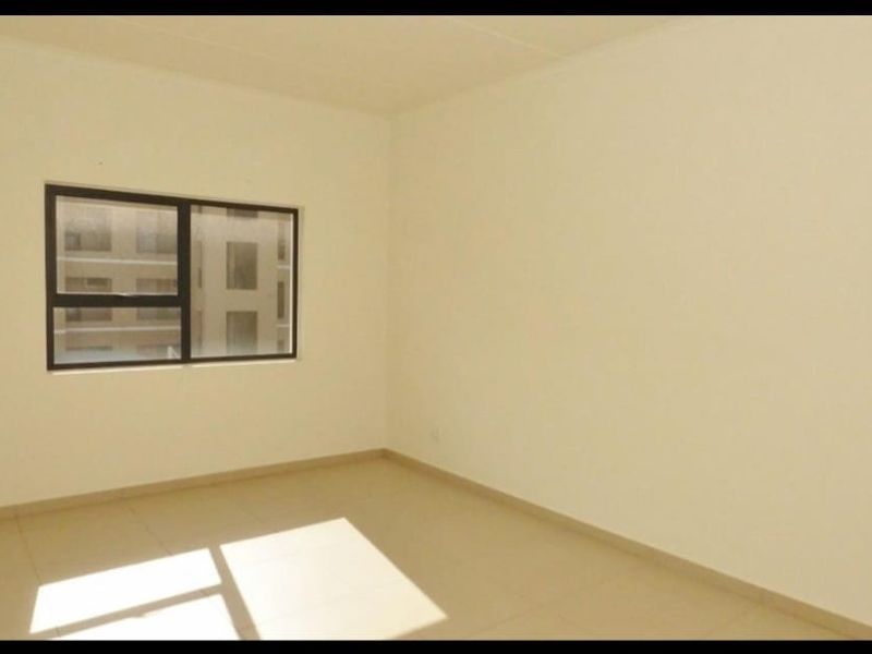 A bright, empty bedroom featuring neutral tiled flooring and a modern aluminium-framed window, providing a clean canvas for personalization.