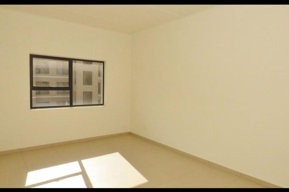 A bright, empty bedroom featuring neutral tiled flooring and a modern aluminium-framed window, providing a clean canvas for personalization.