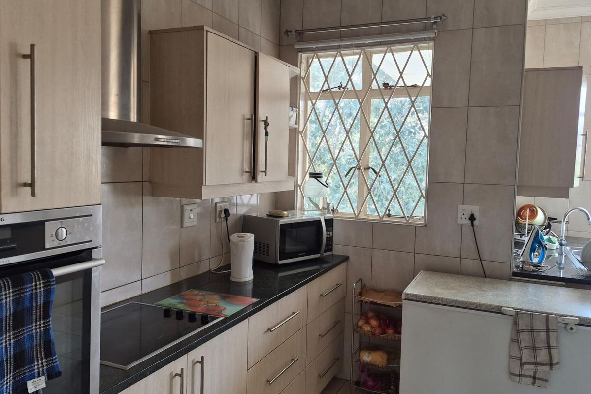A functional kitchen featuring light wood cabinetry, granite countertops, built-in oven, extractor fan, and tiled walls with security-barred windows.