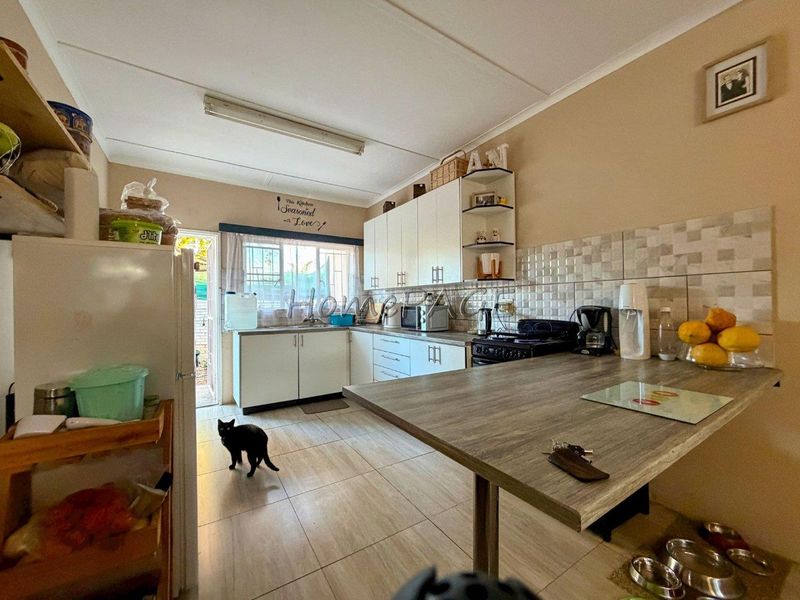A functional kitchen featuring white built-in cabinetry, tiled backsplash, and a breakfast bar area with tiled flooring and direct access to the exterior.