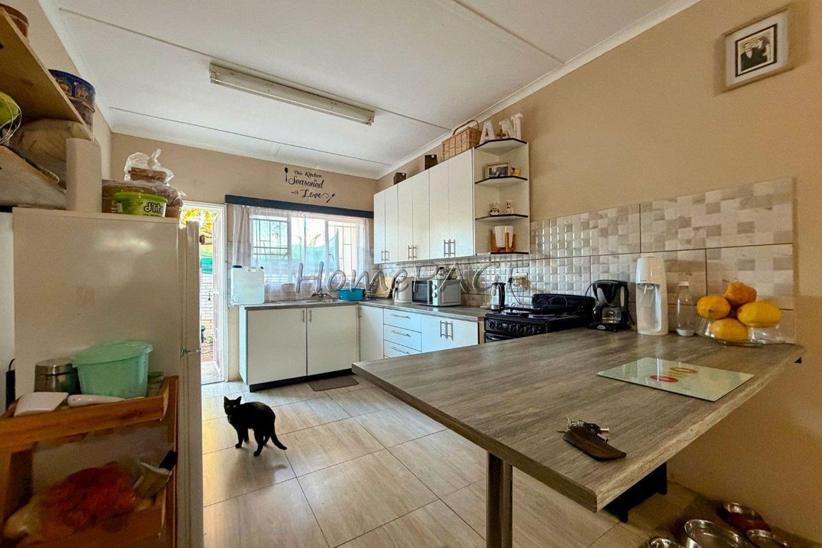 A functional kitchen featuring white built-in cabinetry, tiled backsplash, and a breakfast bar area with tiled flooring and direct access to the exterior.