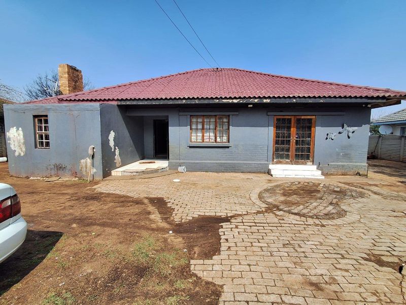 Rear view of a single-story house featuring a paved patio area, timber-framed doors, and a tiled roof, requiring exterior maintenance and cosmetic updates.