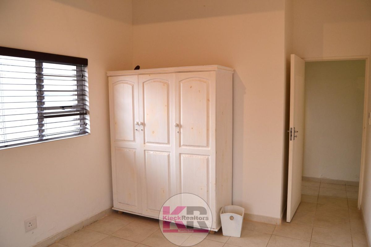A simple bedroom featuring tiled flooring and venetian blinds, providing a neutral space ready for personalization.