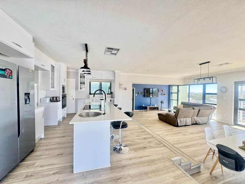 Spacious open-plan living area featuring a modern kitchen with a central island, sleek cabinetry, and seamless flow to the lounge with expansive views.