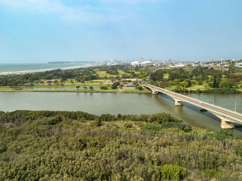 An aerial view showcasing the surrounding landscape, including a river, bridge, and distant coastal city skyline.