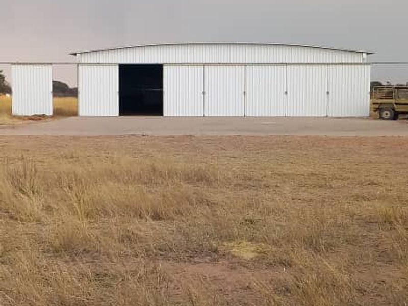 Large industrial-style metal farm shed or hangar featuring sliding doors and a concrete apron, situated on open rural land.