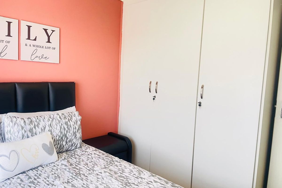 A bedroom featuring built-in white wardrobes and a coral-toned accent wall.