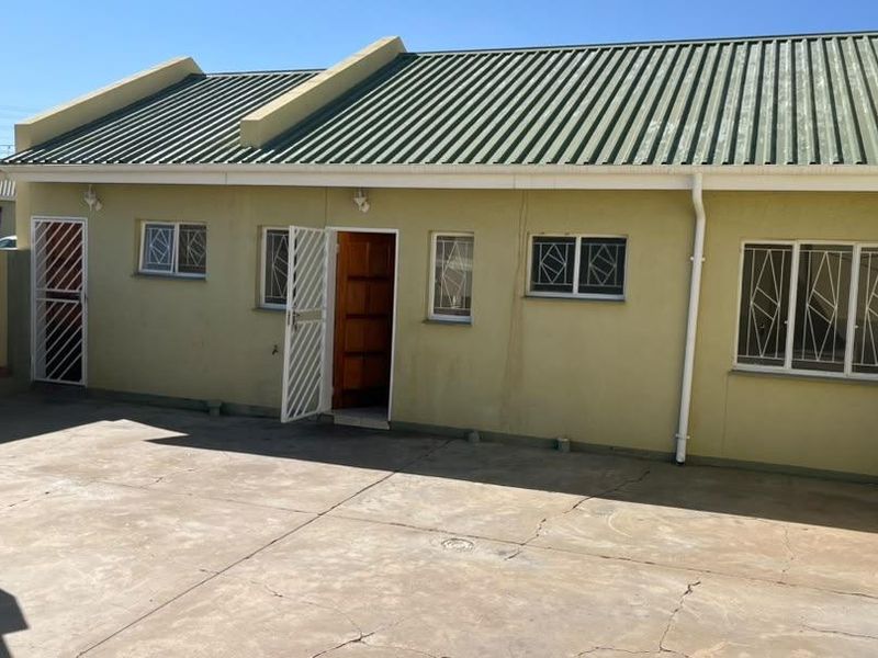 Rear exterior view of the townhouse featuring a concrete patio, built-in braai, and secure access points with burglar bars.
