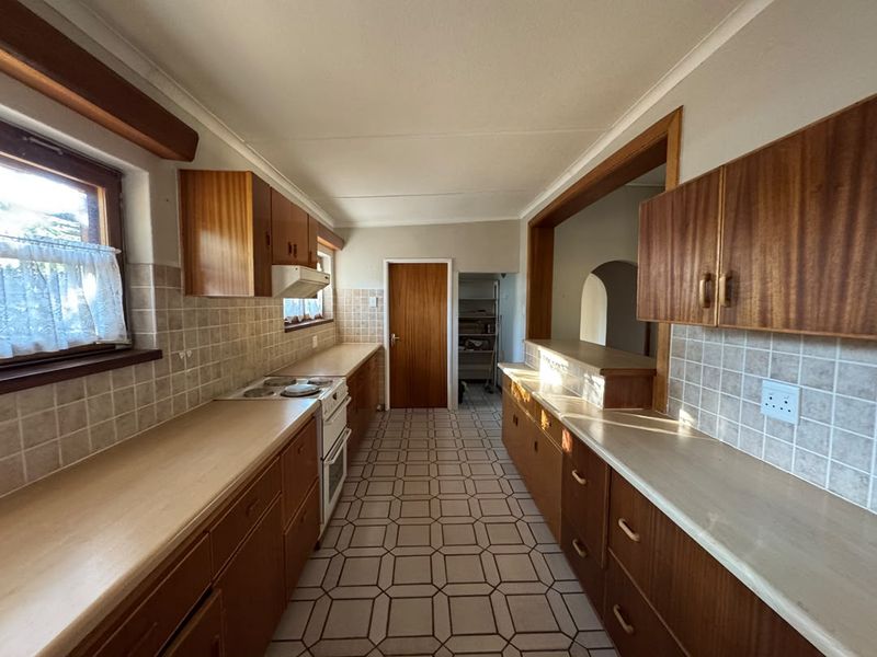 A functional galley-style kitchen featuring original wooden cabinetry, laminate countertops, tiled backsplash, and built-in electric stove with extractor fan.