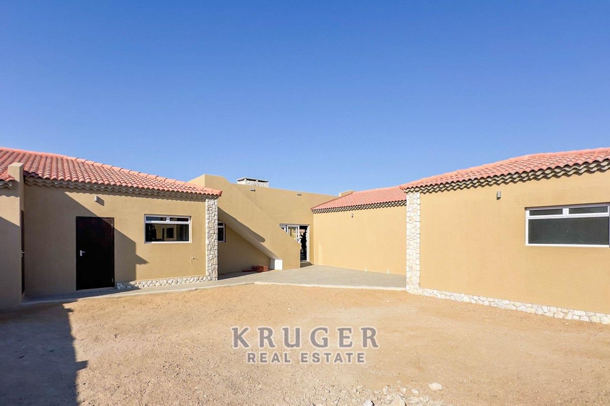 Rear courtyard view of the property featuring terracotta tiled roofing, stone-clad accents, and a clean stucco exterior finish.