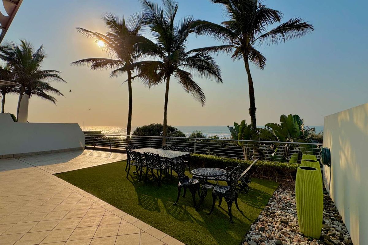 Spacious outdoor patio featuring tiled flooring, artificial grass, and a stainless steel balustrade, offering stunning ocean views and a perfect setting for relaxation.