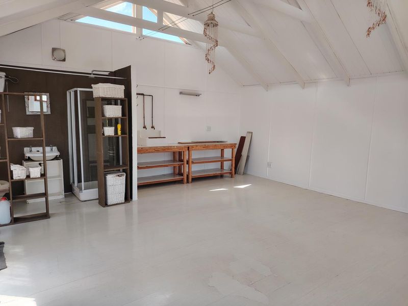 Spacious open-plan area featuring a vaulted ceiling with exposed beams, skylight, integrated shower, and basin, offering a versatile layout with potential for custom finishes.