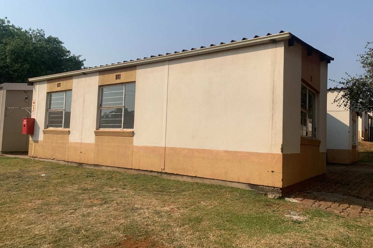 Rear exterior view of a townhouse unit featuring plastered walls, metal-framed windows, and a corrugated metal roof set within a communal garden area.