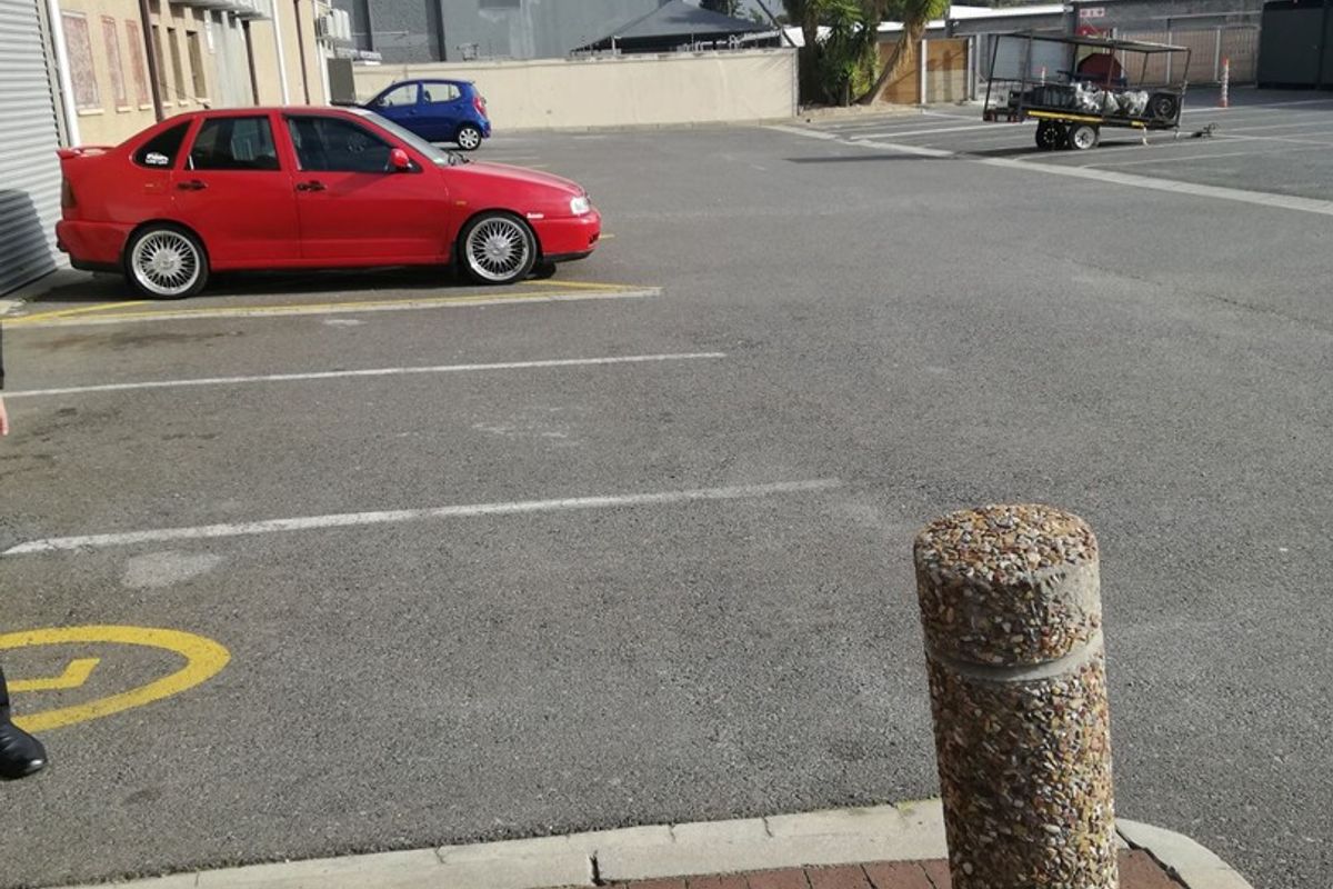 Exterior view of the office property featuring an asphalt parking area, concrete bollards, and brick paving with external air conditioning units.