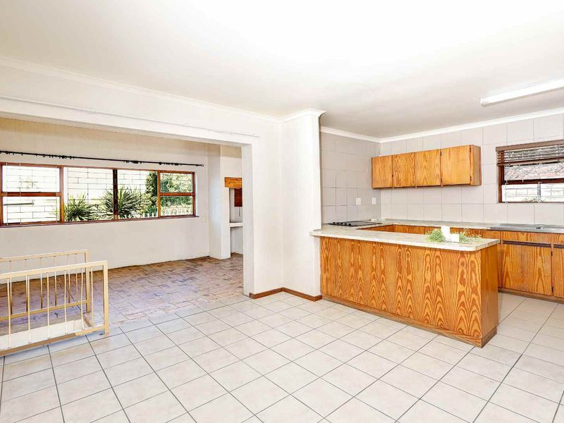 Open-plan kitchen and living area featuring tiled flooring, built-in wooden cabinetry, and a breakfast counter, offering a functional layout with potential for modernization.