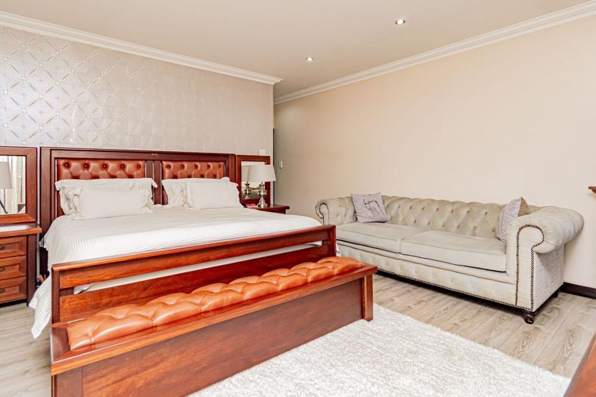 Spacious bedroom featuring laminate flooring, recessed downlighting, and a feature textured wall, providing a comfortable and well-maintained living space.