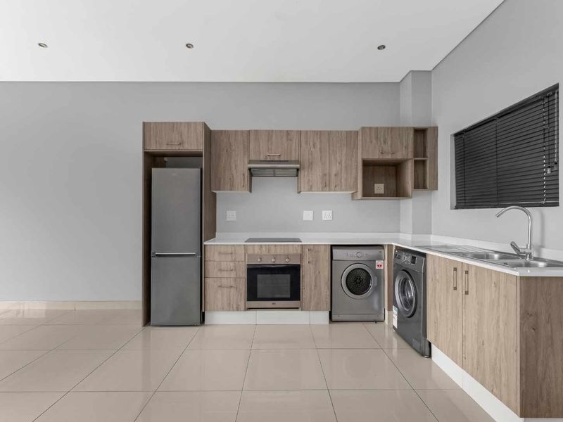 Modern kitchen featuring light wood-grain cabinetry, tiled flooring, integrated oven and hob, and a stainless steel sink with a neutral color palette.