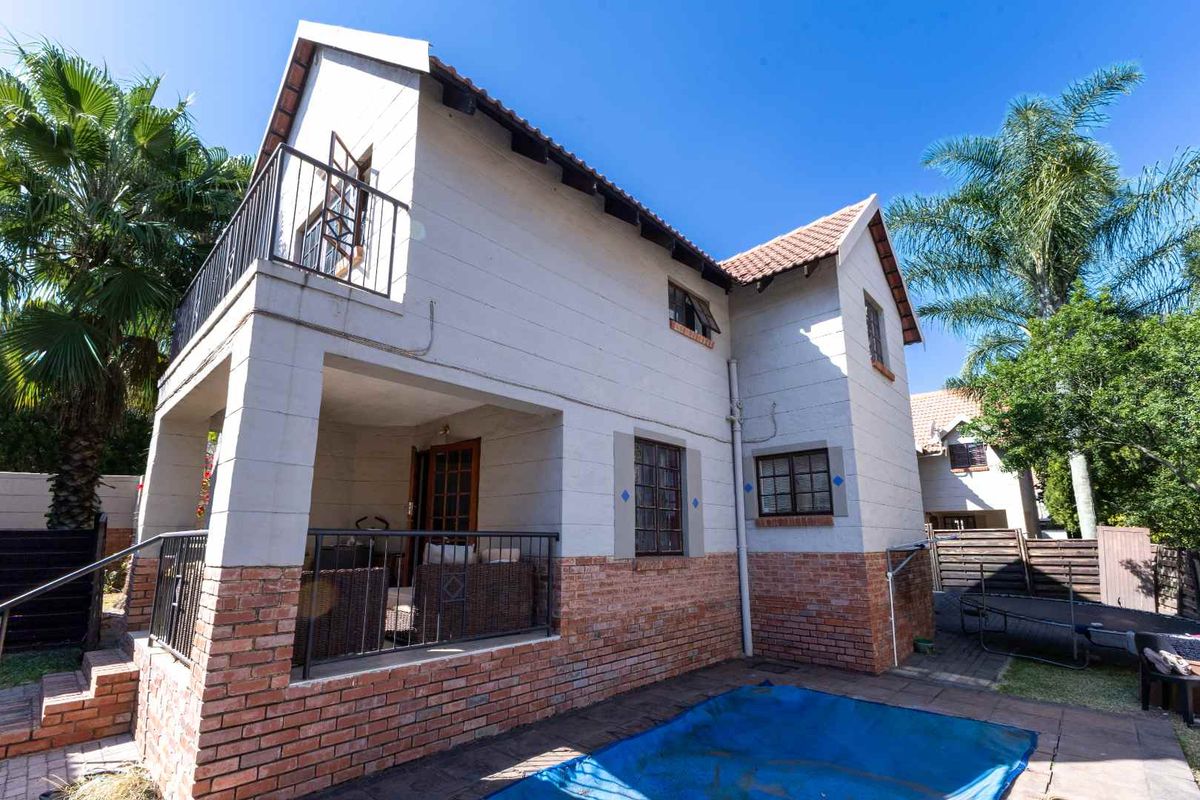 Rear view of the townhouse featuring a covered patio, upper balcony, and a swimming pool set within a private garden area.