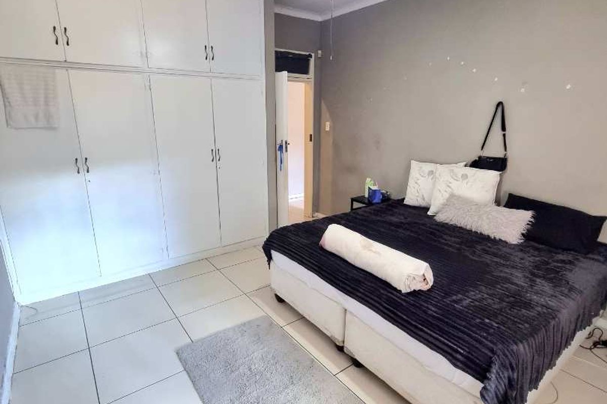 A bedroom featuring built-in floor-to-ceiling cupboards, tiled flooring, and a ceiling fan.