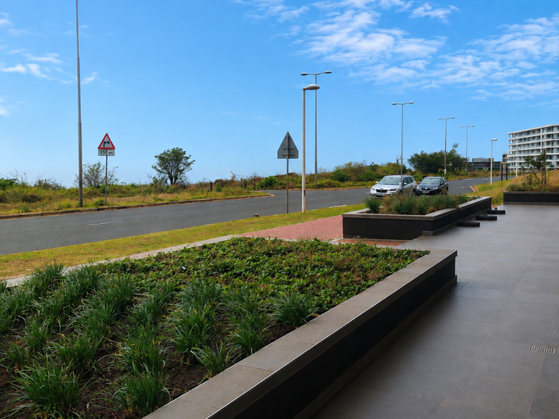 A modern, covered outdoor patio area featuring tiled flooring and integrated raised garden beds, overlooking a street and coastal landscape.