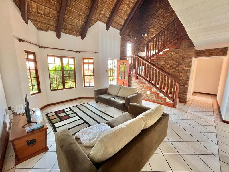 Spacious living room featuring a high thatched ceiling with exposed beams, a striking exposed brick wall, and a wooden staircase.